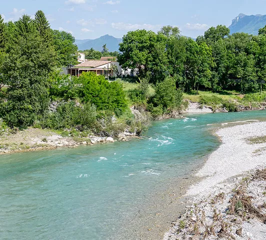 Vue de la rivière Drôme bordée d’arbres et de maisons à Aouste-sur-Sye.