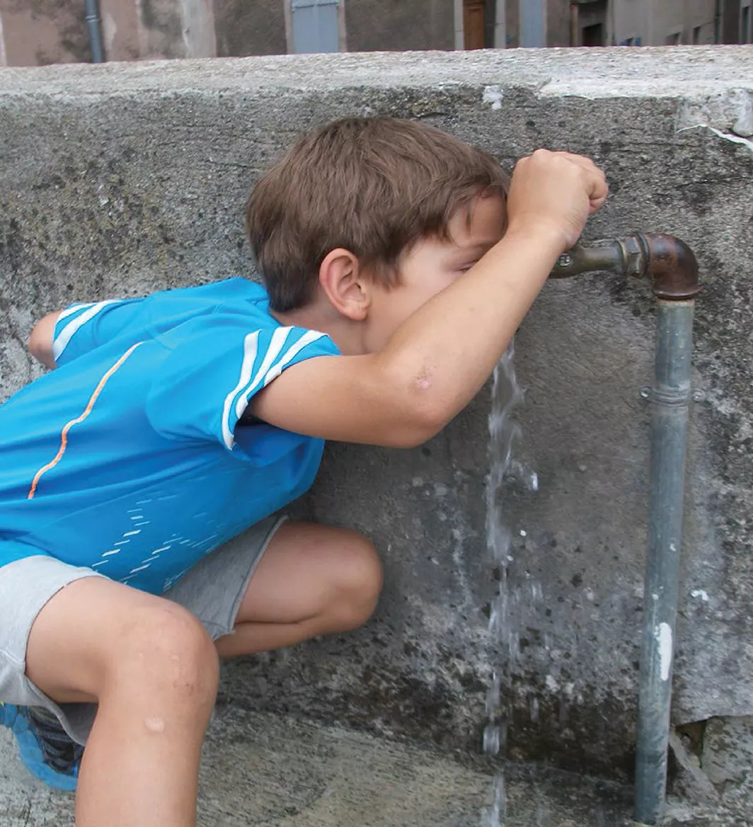 Enfant buvant à une fontaine de village – symbole de l’accès à l’eau potable dans la vallée de la Drôme
